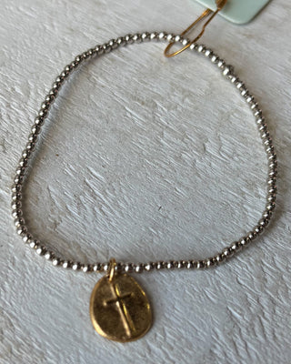 Bracelet with gold cross pendant on a light gray background
