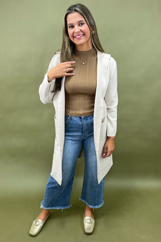 Beige longline cardigan layered over ribbed camel top styled with light wash wide leg jeans and gold loafers