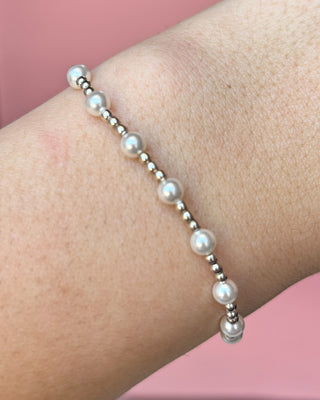 Pearl bracelet on a wrist against a pink background