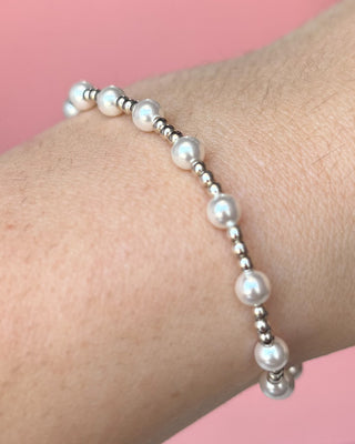 Pearl bracelet on a wrist with a pink background