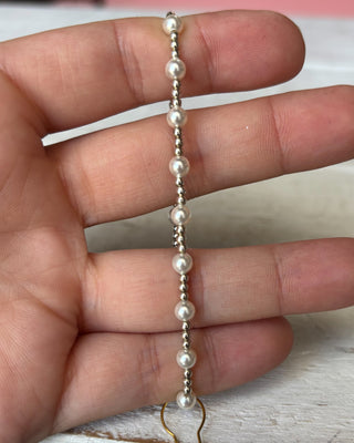 Pearl necklace held between fingers on a neutral background