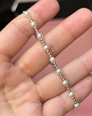 Pearl necklace held between fingers against a blurred background