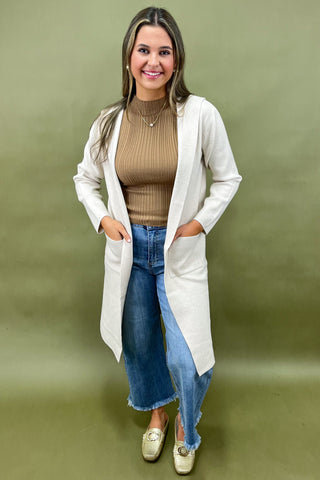 Beige longline cardigan layered over ribbed camel top styled with light wash wide leg jeans and gold loafers