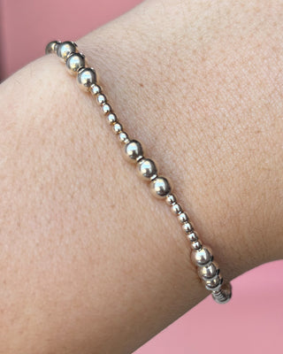 Silver beaded bracelet on a wrist with a pink background