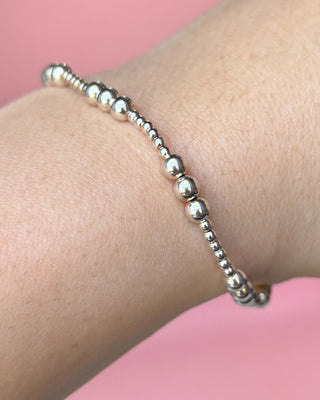 Silver beaded bracelet on a wrist with a pink background