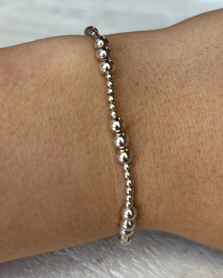 Silver beaded bracelet on a wrist against a neutral background