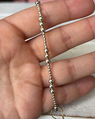 Silver beaded bracelet held between fingers on a light background