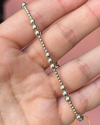 Silver beaded necklace on a hand with a pink background
