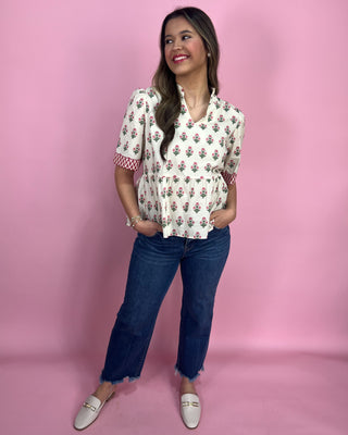 Woman wearing a floral blouse and jeans against a pink background