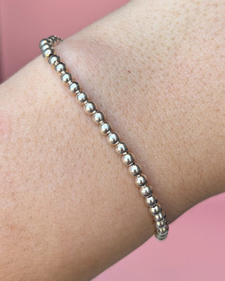 Silver beaded bracelet on a wrist against a pink background