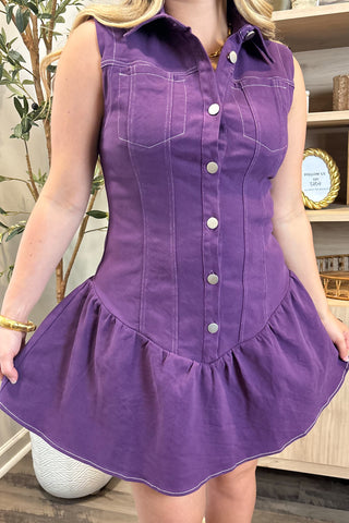 Person wearing a purple dress with a button-up front in an indoor setting.