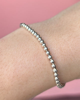 Silver beaded bracelet on a wrist with a pink background