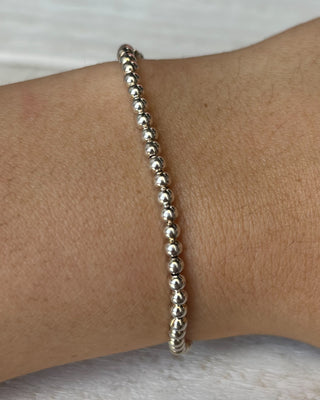 Silver beaded bracelet on a wrist against a neutral background