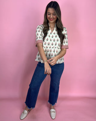 Woman wearing a floral blouse and blue jeans against a pink background