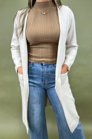Beige longline cardigan layered over ribbed camel top styled with light wash wide leg jeans and gold loafers
