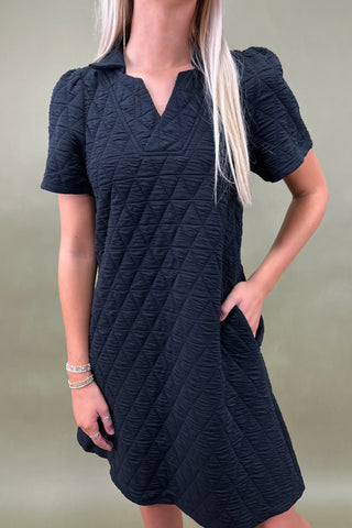 Woman wearing a black textured dress against a plain background