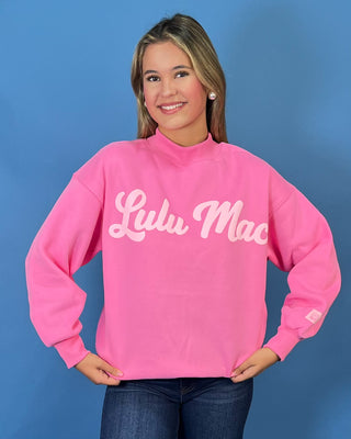 Pink LULU MAC graphic sweatshirt with long sleeves and crew neckline, styled with dark wash wide leg jeans.