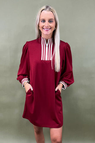 Woman wearing a burgundy dress with white stripes on a plain background