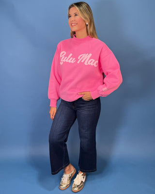 Pink LULU MAC graphic sweatshirt with long sleeves and crew neckline, styled with dark wash wide leg jeans.