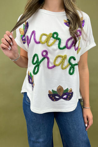 White t-shirt with colorful 'Mardi Gras' text and mask design worn by a person against a green background