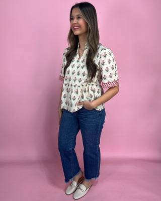 Woman wearing a floral blouse and blue jeans against a pink background