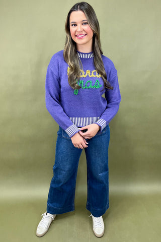 Woman wearing a purple sweater with text and blue jeans on a green background