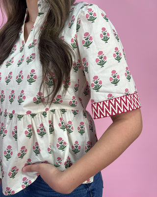 Woman wearing a white blouse with pink floral pattern and red embroidery on a pink background