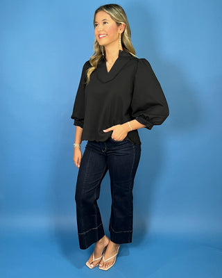 Black scalloped blouse with a split neckline, puff sleeves, scalloped trim, and a polished feminine fit.