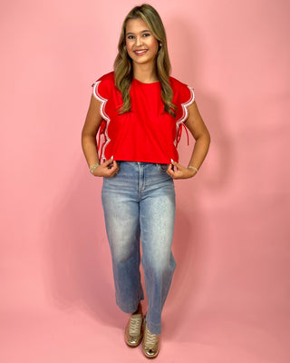 Woman wearing a red top with white trim and blue jeans on a pink background