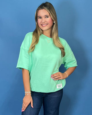 Mint green LULU MAC short sleeve top with a relaxed fit, styled with dark wash wide leg jeans.