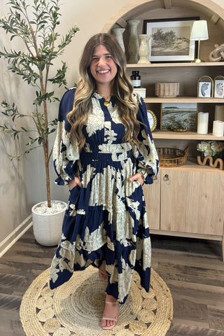 Woman wearing a blue and white floral dress in a room with a plant and shelves.