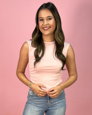 Light blush sleeveless fitted tank top with a smooth, stretchy finish, paired with cropped wide leg denim jeans and neutral wedge sandals, styled against a pink backdrop.