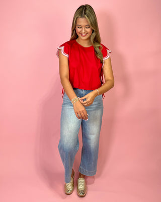 Woman wearing a red top with white trim and blue jeans on a pink background