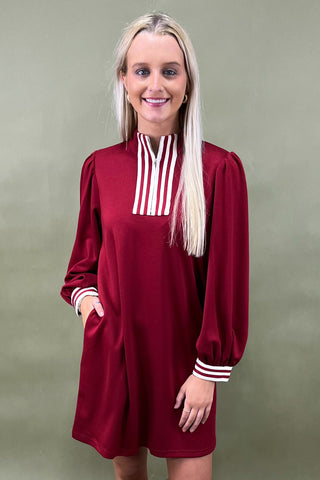 Woman wearing a burgundy dress with a white and red striped collar against a green background