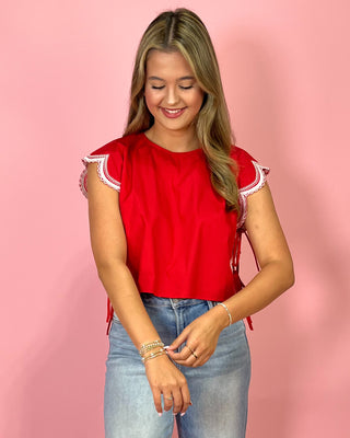 Woman wearing a red top with lace sleeves against a pink background