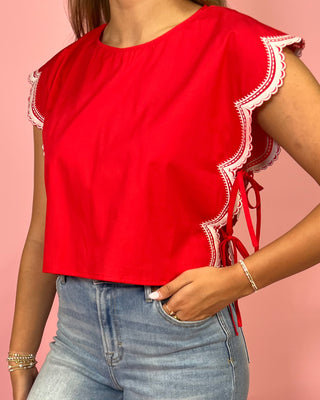 Red top with lace details worn by a person on a pink background