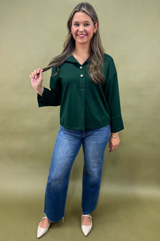 Woman wearing a green blouse and blue jeans against a beige background