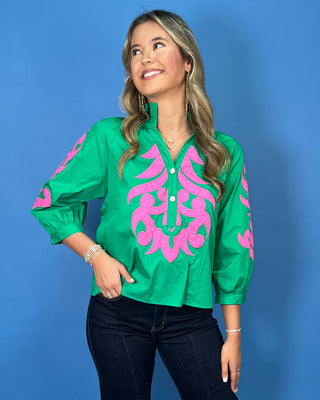 Green blouse with bright pink embroidered detailing, button neckline, and three-quarter puff sleeves.