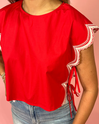 Red blouse with white lace details on sleeves against a pink background