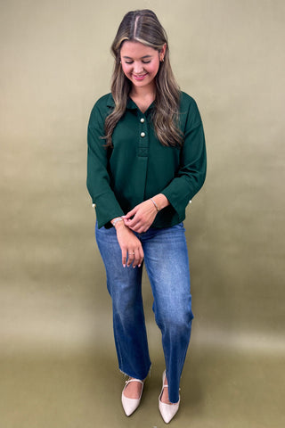Woman wearing a green shirt and blue jeans against a beige background