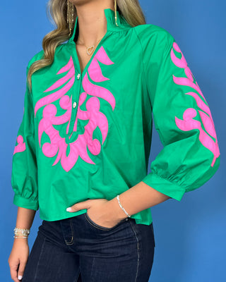 Green blouse with bright pink embroidered detailing, button neckline, and three-quarter puff sleeves.