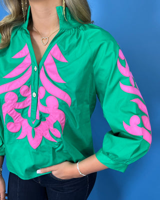 Green blouse with bright pink embroidered detailing, button neckline, and three-quarter puff sleeves.