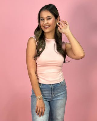 Light blush sleeveless fitted tank top with a smooth, stretchy finish, paired with cropped wide leg denim jeans and neutral wedge sandals, styled against a pink backdrop.