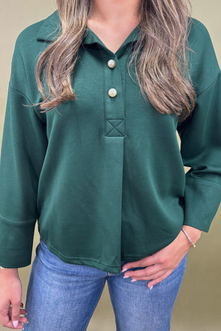 Person wearing a green blouse with long sleeves and a neutral background
