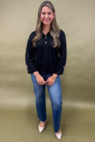 Woman wearing a black blouse and blue jeans against a beige background