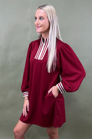 Woman wearing a burgundy dress with white stripes on a plain background
