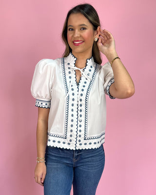 Woman wearing a white blouse with black embroidery against a pink background
