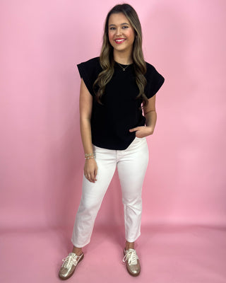 Woman wearing a black top and white pants against a pink background