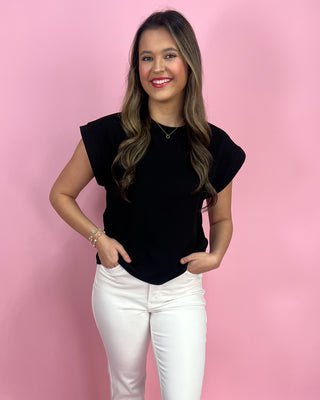 Woman wearing a black top and white pants against a pink background
