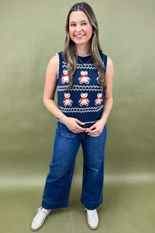 Woman wearing a sleeveless sweater with a pattern of bears and text, standing against a green background.
